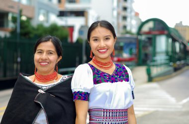 Güzel İspanyol anne ve kızı geleneksel And giysileri giyen, birlikte poz verirken kamu istasyonunda otobüs bekliyor, mutlu, açık havada çevre gülümseyerek