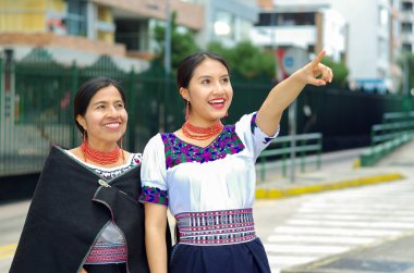 Güzel İspanyol anne ve kızı geleneksel And giysileri giyen, kamu istasyonunda otobüs beklerken etrafında işaret ederken, mutlu, açık havada çevre gülümseyerek