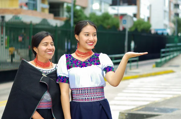 Hermosa madre e hija hispanas vestidas con ropa andina tradicional, esperando el autobús en la estación pública mientras interactúan juntas, sonriendo felizmente, al aire libre —  Fotos de Stock