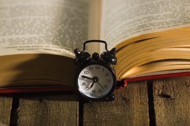Ahşap yüzey, eski moda gece masa saati yanındaki oturma, sihirli kavramı ateş aç yatan kalın bir kitap