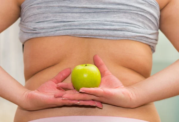 Primeros planos de las mujeres de la parte inferior de la espalda con la camisa levantada, con pantalones vaqueros, la celebración de manzana entre las manos, concepto de pérdida de peso — Foto de Stock