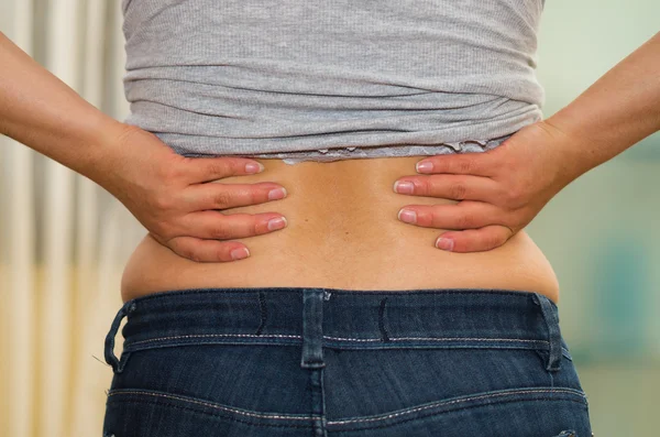 Closeup womans lower back with shirt lifted up, wearing jeans, holding hands on hips, weightloss concept — Stock Photo, Image