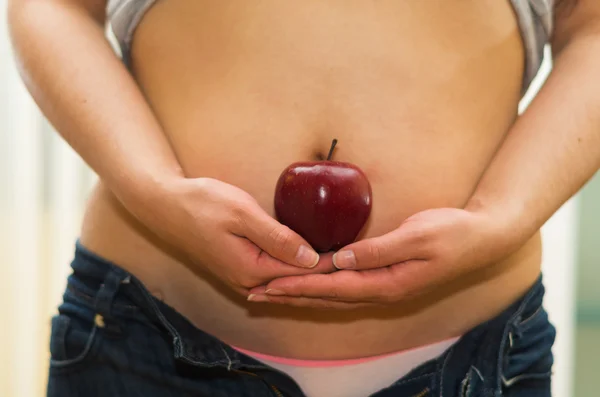 Closeup womans stomach with unzipped jeans and shirt lifted up, holding apple between hands, underwear visible, weightloss concept — Stock Photo, Image