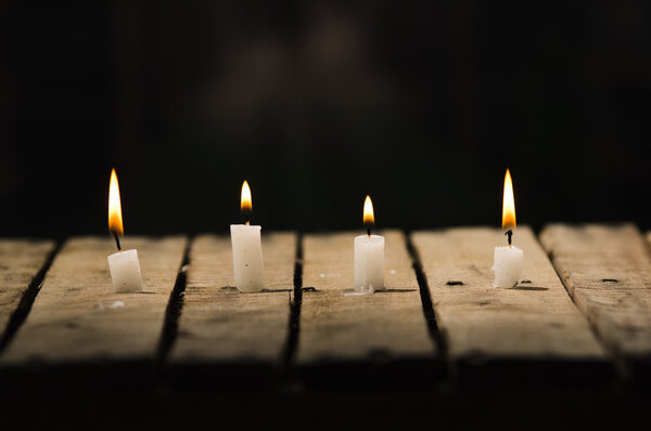 Four white wax candles sitting on wooden surface burning with black background, beautiful light setting
