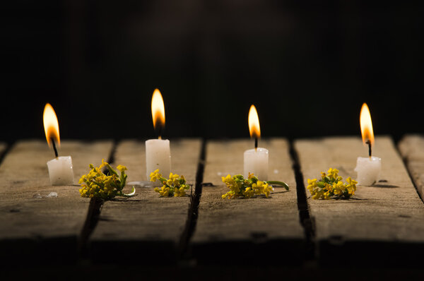 Four white wax candles sitting on wooden surface burning with black background, beautiful light setting