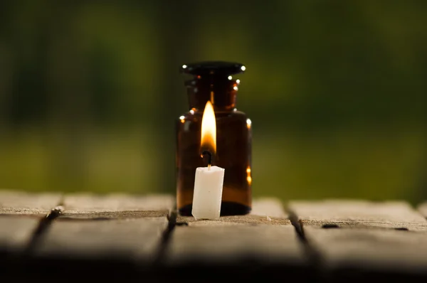 Pequena garrafa de remédio marrom para mágicos remédio e vela de cera branca sentado na superfície de madeira, belo cenário de luz noturna, conceito mágico — Fotografia de Stock