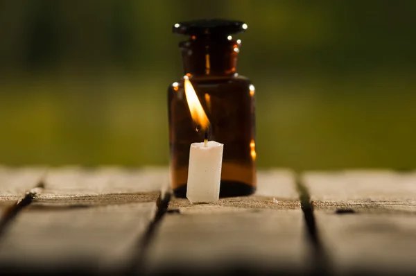 Small brown medicine bottle for magicians remedy and white wax candle sitting on wooden surface, beautiful night light setting, magic concept — Stock Photo, Image
