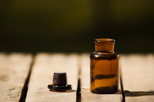 Pequena garrafa de remédio marrom para mágicos remédio, tampa preta deitada ao lado dele na superfície de madeira — Fotografia de Stock