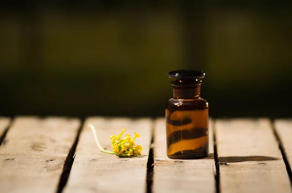 Pequena garrafa de remédio marrom para mágicos remédio, flor amarela deitada ao lado dele, sentado na superfície de madeira — Fotografia de Stock