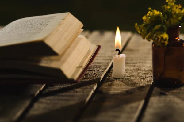 Libro spesso sdraiato aperto sulla superficie di legno, candela di cera e piccola bottiglia con fiori gialli seduti accanto ad essa, bella impostazione della luce notturna, concetto magico sparare — Foto Stock