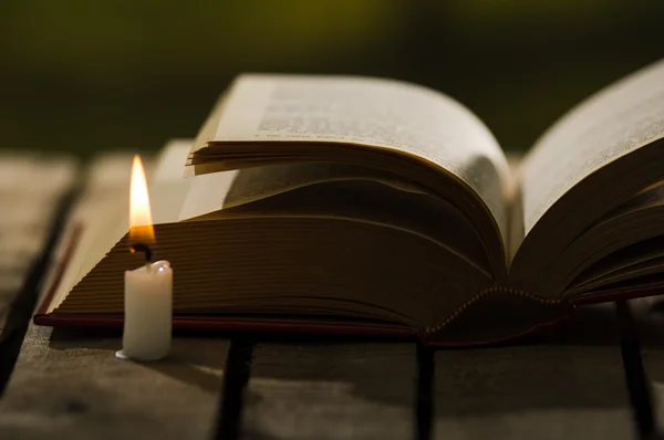 Vastag könyv feküdt nyitott fa felület, viasz gyertyát ül mellette, beállítás, gyönyörű éjszakai fény lő mágikus koncepció — Stock Fotó
