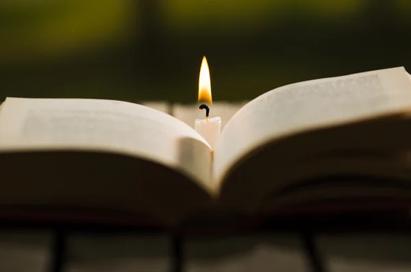 Dickes Buch offen auf Holzoberfläche liegend, Wachskerze daneben sitzend, wunderschöne Nachtbeleuchtung, magisches Konzeptshooting — Stockfoto