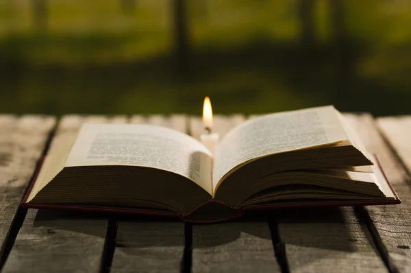 Thick book lying open on wooden surface, wax candle sitting next to it, beautiful night light setting, magic concept shoot — Stock Photo, Image