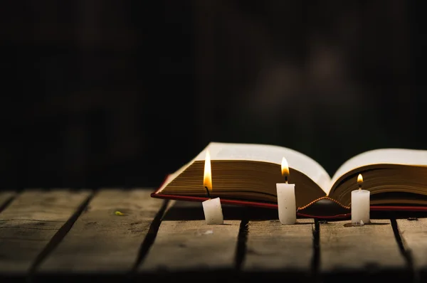 Libro grueso que miente abierto en la superficie de madera, velas de cera colocadas en frente, ajuste hermoso de la luz de la noche, lanzamiento mágico del concepto — Foto de Stock