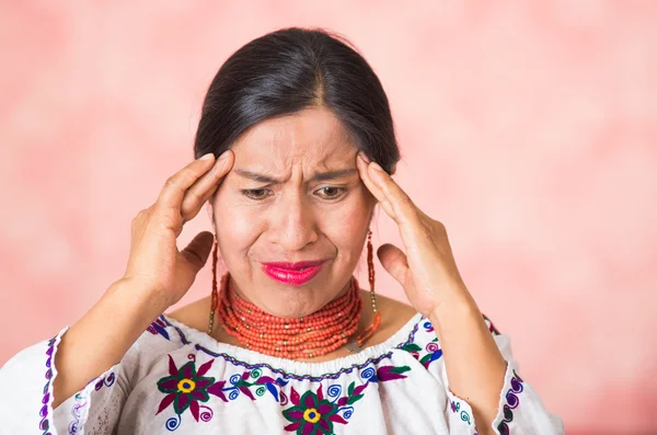 Headshot όμορφη Ισπανόφωνος μητέρα φορώντας παραδοσιακές των Άνδεων ενδύματα, προσομοιώνοντας πονοκέφαλο χρησιμοποιώντας τα χέρια που αγγίζουν το μέτωπο, επώδυνη έκφραση του προσώπου, φόντο ροζ στούντιο — Φωτογραφία Αρχείου