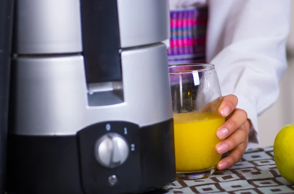 Closeup exclusive juice maker sitting on table, hand holding onto glass of yellow liquid — Stock Photo, Image