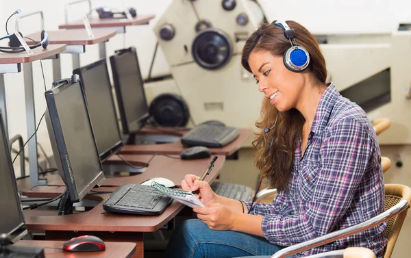 Young lady taking notes while talking with someone on the headset — Stock Photo, Image