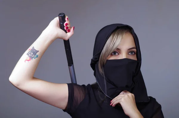 Samurai kvinna klädd i svart med matchande slöja som täcker ansiktet, holding arm på svärdet gömt bakom ryggen, mot kameran, ninja koncept — Stockfoto