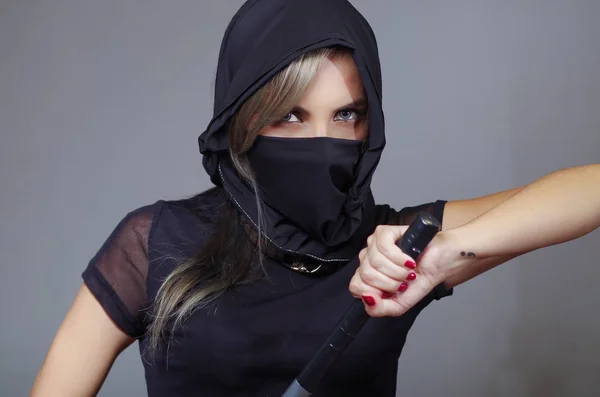 Samurai mujer vestida de negro con velo a juego cubriendo la cara, sosteniendo la mano en la espada frente a la cámara, concepto ninja — Foto de Stock