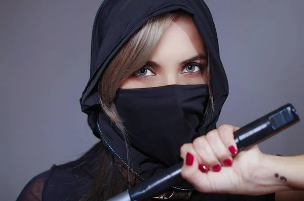Femme samouraï vêtue de noir avec voile couvrant le visage correspondant, tenant la main sur l'épée face à la caméra, concept ninja — Photo