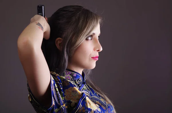 Samurai mujer vestida con tradicional patrón de flores de colores vestido de seda asiática, la celebración de brazo sobre el hombro agarrando espada oculta detrás de la espalda, frente a la cámara, concepto ninja — Foto de Stock