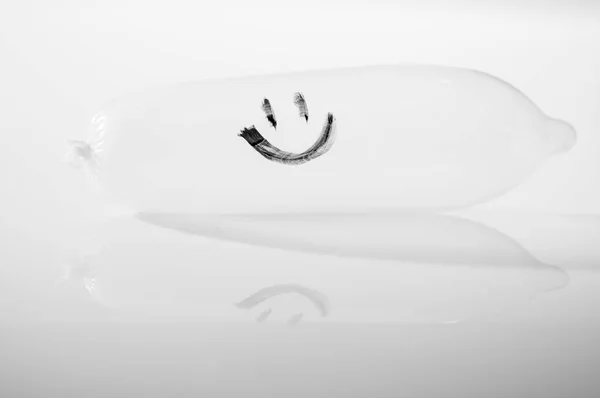 Primo piano preservativo trasparente pieno di aria e faccina sorridente disegnato, sdraiato sulla superficie bianca, sfondo studio, concetto di sicurezza sessuale , — Foto Stock