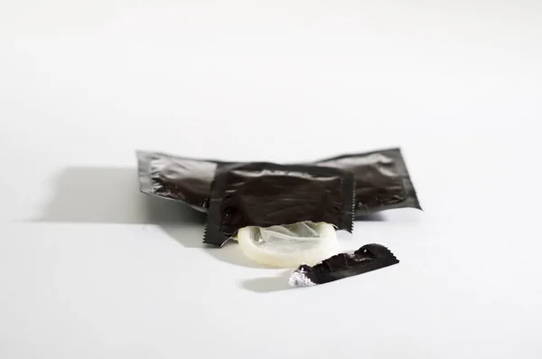 Closeup transparent condom as seen sticking out of the packaging lying on white surface, studio background, safe sex concept — Stock Photo, Image