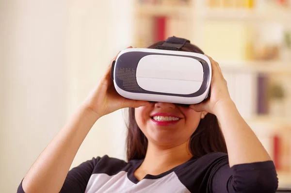 Mujer morena joven con gafas de realidad virtual experimentando la tecnología del futuro, interactuando y sonriendo mientras juega, fondo doméstico, concepto vr —  Fotos de Stock