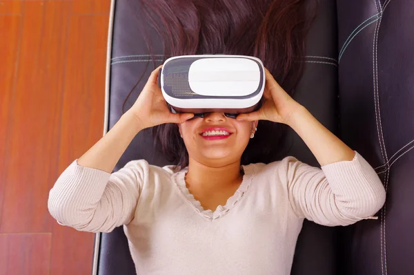 Młoda brunetka kobieta leżąc sobie wirtualnej rzeczywistości gogle przeżywa przyszłych technologii, interakcji i uśmiechając się podczas gry, koncepcja vr, — Zdjęcie stockowe