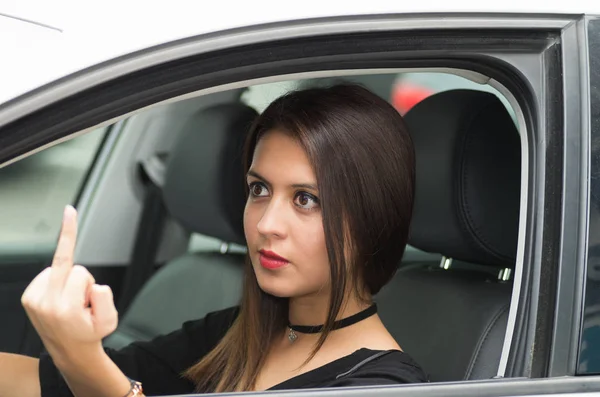 Primeros planos mujer joven sentada en el coche dando el dedo airadamente, como se ve desde la ventana de los conductores exteriores, concepto de conductor femenino —  Fotos de Stock