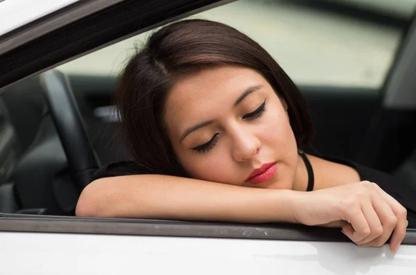 Closeup young woman sitting in car interacting tired and sleeping, as seen from outside drivers window, female driver concept — Stock Photo, Image