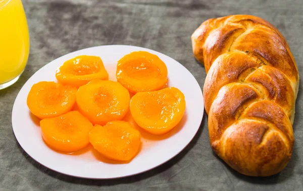 Крупним планом свіжоспечений цукровий хліб з красивим золотистим кольором, біла тарілка нарізаних персиків, концепція хлібобулочних виробів — стокове фото