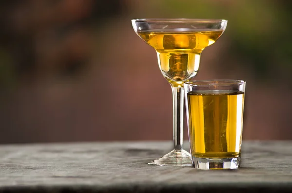 Classy cocktail glass sitting on grey surface, yellow liquid inside with blurry urban background — Stock Photo, Image