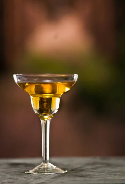 Шикарное коктейльное стекло сидит на серой поверхности, желтая жидкость внутри с размытым городским фоном — стоковое фото