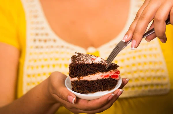 Donna che tiene piccolo piatto di torta al cioccolato con ripieno di crema, afferrando il morso con la forchetta, mostrando alla macchina fotografica, concetto di pasticceria — Foto Stock