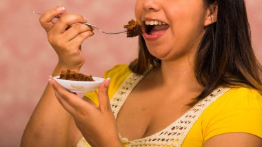 Kamera, pasta kavramı gösterilen çatal kullanarak ısırık kapma çikolatalı browni kek, küçük tabak tutan esmer kadın