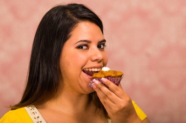 Bir ısırık, pasta kavramı almak için lezzetli kahverengi renkli kek krem tepesi, kocaman bir gülümseme ile hazır tutan esmer kadın