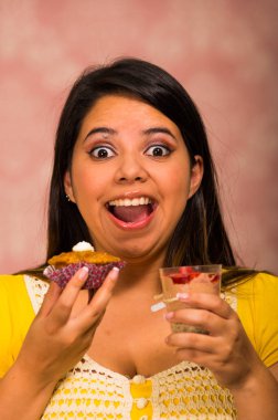 Lezzetli kahverengi renkli kek krem tepesi, diğer el, kocaman bir gülümseme ve bir ısırık, pasta kavramı almaya hazır köpük bardak tutan esmer kadın