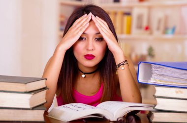 Üzerine kafa, elele pembe en iyi oturma Masası üzerinde yerleştirilir kitap yığını ile tarafından giyen genç esmer kadın yorgun yüz ifadesi ve bodu dil, öğrenci kavramı