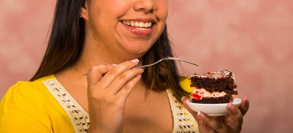 Brunette woman holding small plate of chocolate cake with cream filling, grabbing bite using fork, showing to camera, pastry concept — Stock Photo, Image