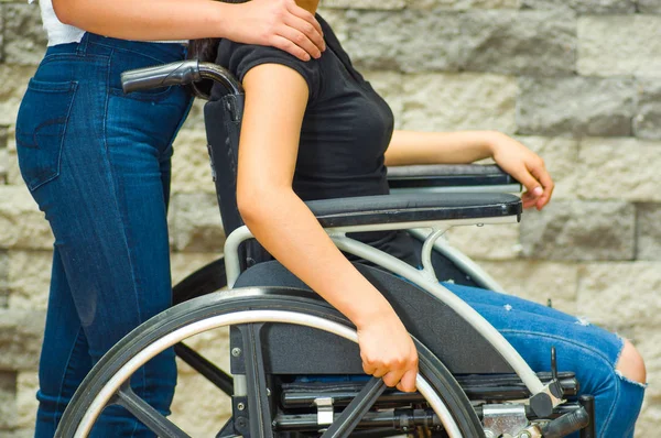 Молода жінка сидить у інвалідному кріслі з помічником, що стоїть поруч з нею, і посміхається щасливо демонструючи позитивне ставлення, концепція фізичного одужання — стокове фото