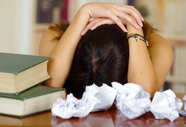 年轻的黑发女人，身穿粉色上衣躺弯曲在写字台上的一摞书放在上面，浪费论文周围，似乎睡着了，累了的学生概念 — 图库照片
