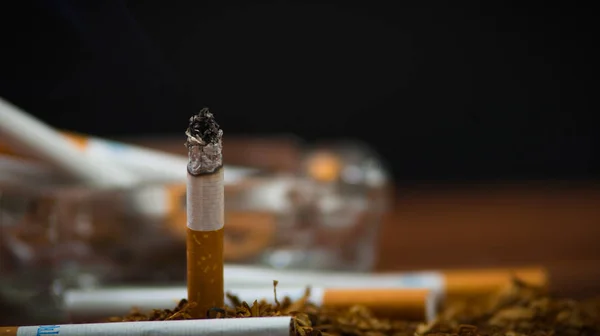 Closeup cigarettes and tobacco lying inside and around glass ash tray on wooden surface, anti smoking concept — Stock Photo, Image