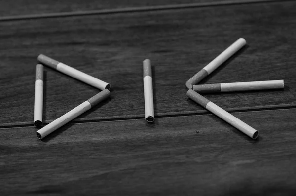 Cigarettes lying on wooden surface shaped into the word die, artistic anti smoking concept, black and white edition — Stock Photo, Image