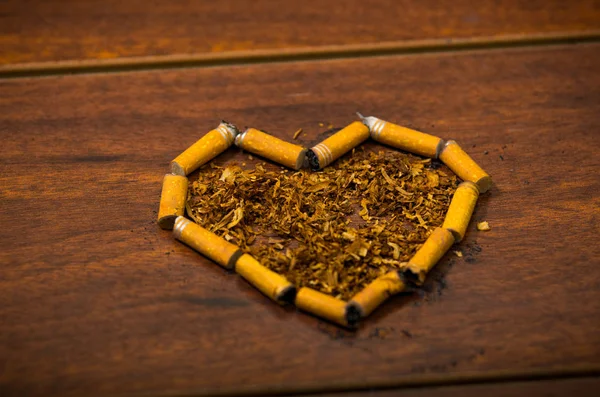 Cigarette butts shaped into a heart lying on wooden surface, tobacco spread around middle, seen from above — Stock Photo, Image