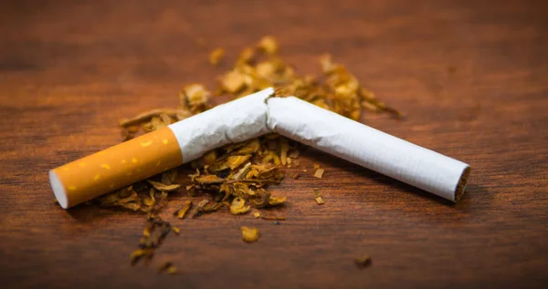 Closeup broken cigarette and tobacco lying on wooden surface, smoking concept — Stock Photo, Image