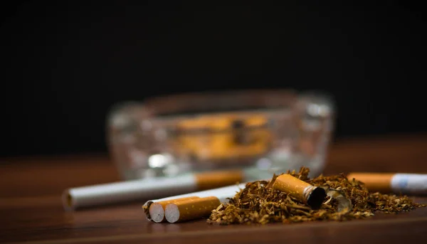 Closeup cigaret a tabáku ležící uvnitř a v okolí skleněný popelník na dřevěnou desku, anti kouření koncept — Stock fotografie