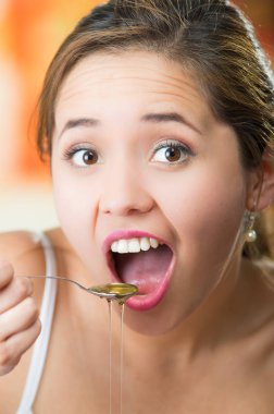 Genç kadın bakan kamera tutarak kaşıkla kenar üzerinde damlayan bal, ağzı açık olarak yemeye hazır