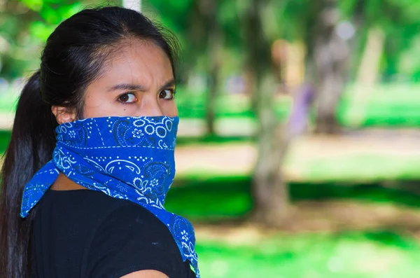 Mujer morena joven con bandana azul cubriendo la mitad de la cara, interactuando al aire libre para la cámara, concepto de protesta activista — Foto de Stock