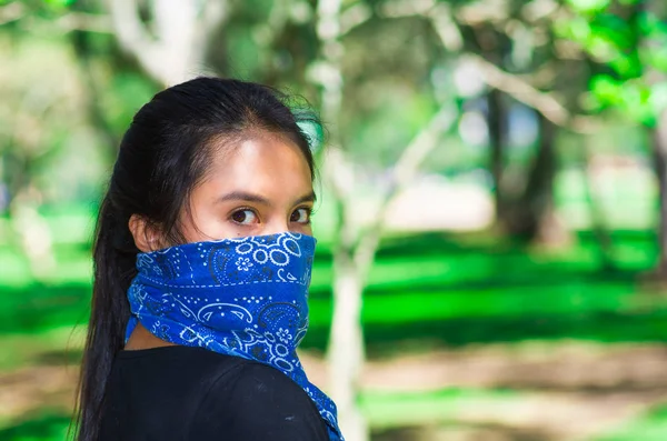 Mujer morena joven con bandana azul cubriendo la mitad de la cara, interactuando al aire libre para la cámara, concepto de protesta activista — Foto de Stock